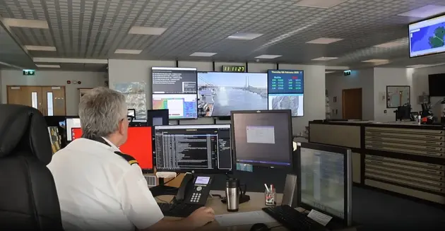 Maritime operations officer monitoring vessel activity and live camera feeds on multiple control-room screens.