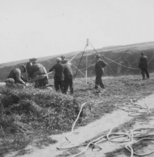 Historic black-and-white photograph showing personnel using ropes and equipment during an early coastal rescue operation.