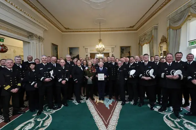Large group of uniformed personnel assembled indoors for a formal ceremony, with an individual holding a certificate at the centre.