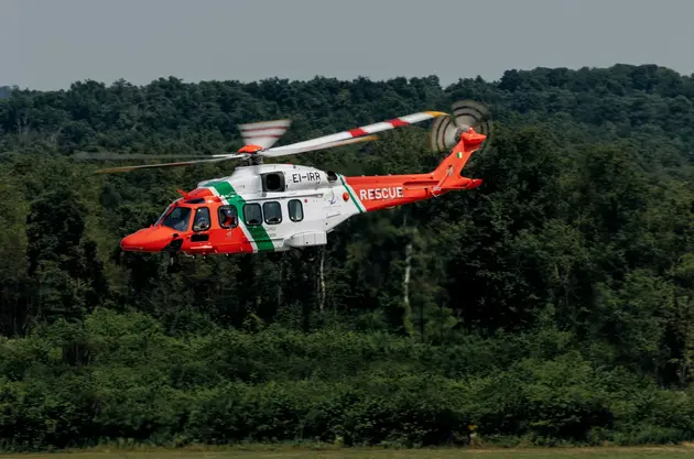 Rescue helicopter flying at low altitude over land, with forested terrain in the background