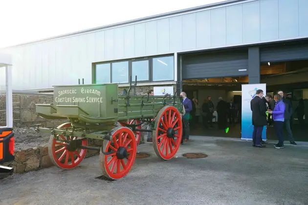 Cairt stairiúil tarrthála a tharraing capaill, agus í ar taispeáint taobh amuigh de shaoráid chósta nua-aimseartha, agus daoine cruinnithe in aice láimhe.