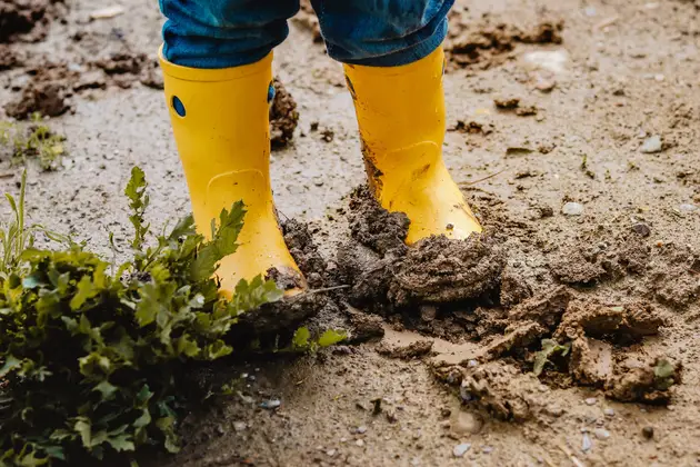 Lower legs wearing yellow waterproof boots standing in soft, muddy ground with waterlogged sand around the feet.