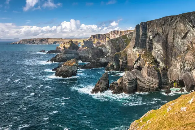 Rugged coastal cliffs rising from the sea, with waves breaking against exposed rock formations below.