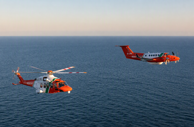 A rescue helicopter and a fixed wing aircraft flying over open sea during a coordinated aerial operation.