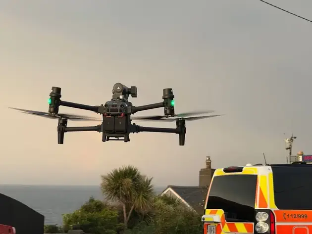 Small quadcopter drone in flight, with a mounted camera visible underneath.