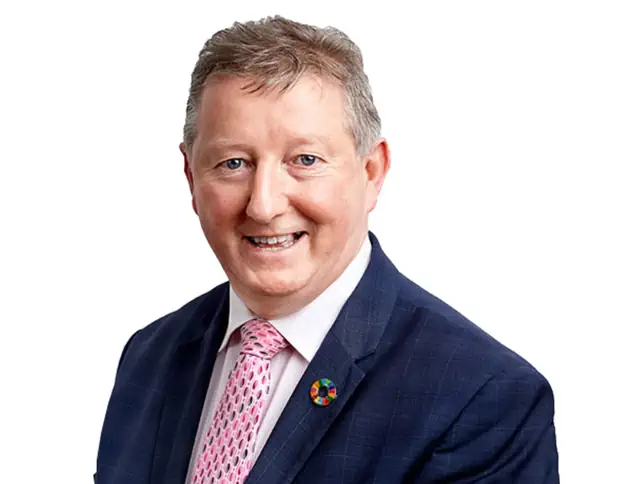 Formal head and shoulders portrait of Minister Sean Canney wearing a suit and patterned tie against a plain white background